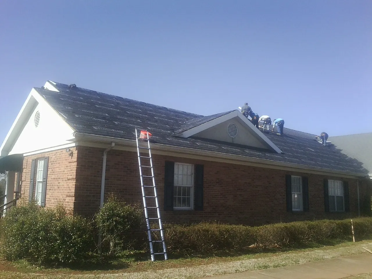 Crew tearing shingles off a brick ranch roof with a ladder set — Emergency Roof Repair work by our crew in Raritan