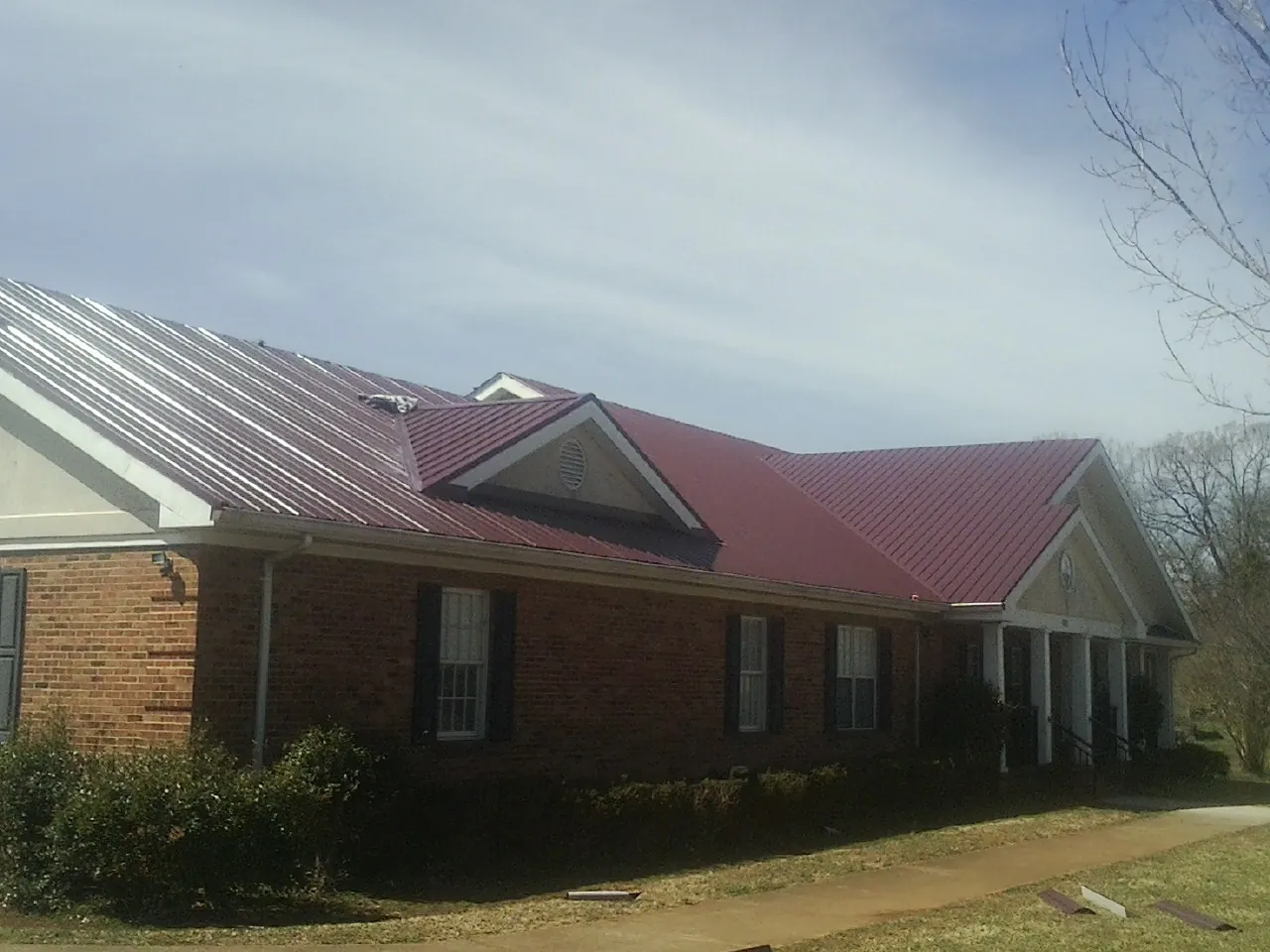 Red metal roof with gabled entries on a long brick building, from a Hail Damage Roof Repair job in Raritan