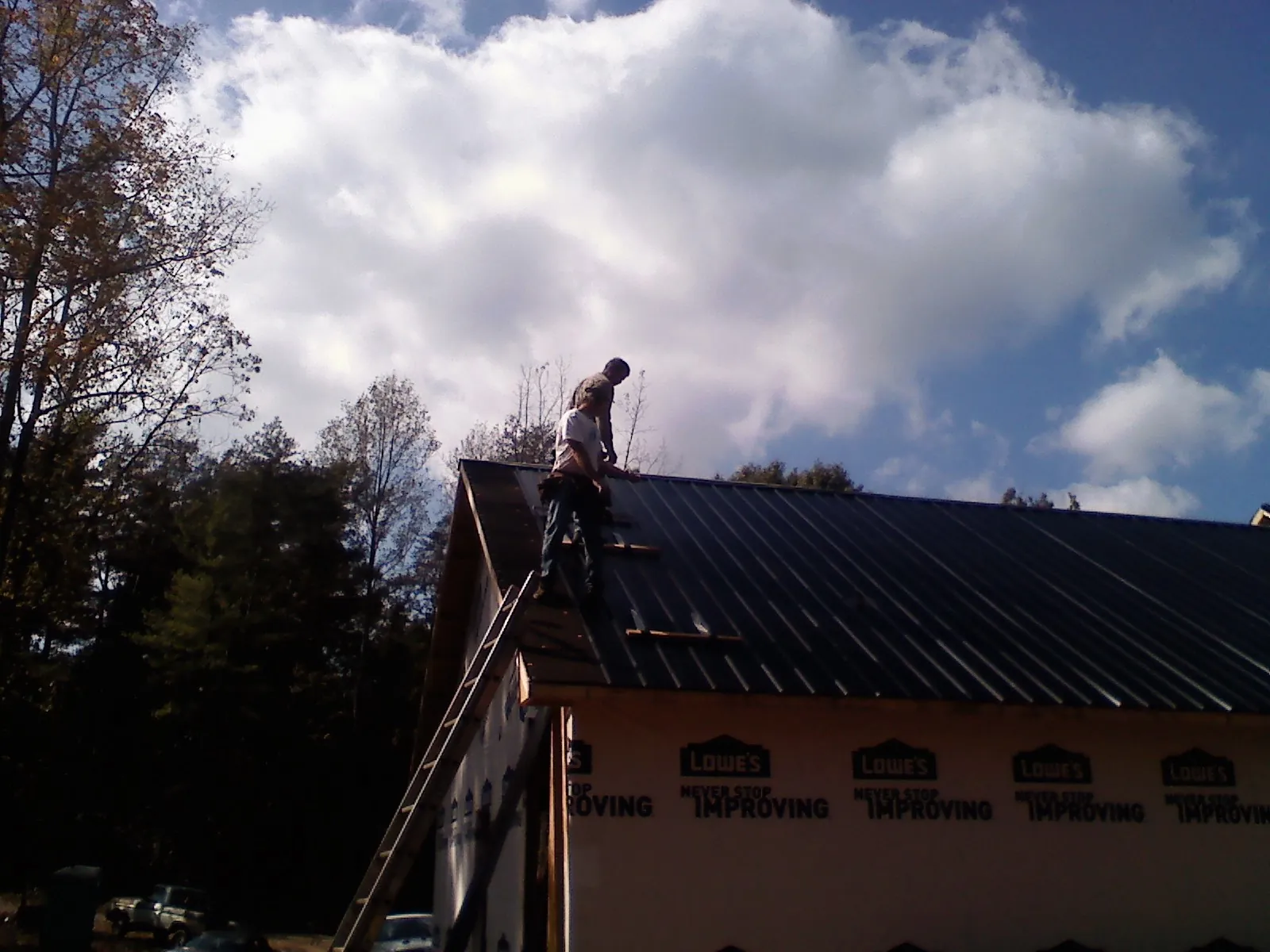 Roofer fastening dark metal panels high against a cloudy sky, from a Roof Inspection job in Raritan