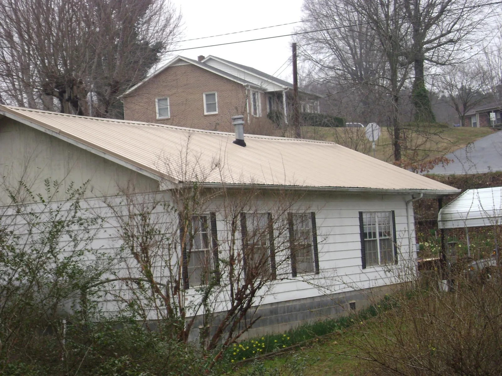 Tan metal roof on a white sided house set into a hillside — Commercial Roofing by Roofing Brothers in Raritan